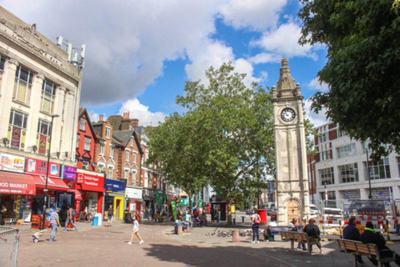 Lewisham clock tower on a sunny day, with blue sky and the shops to the left of the photo